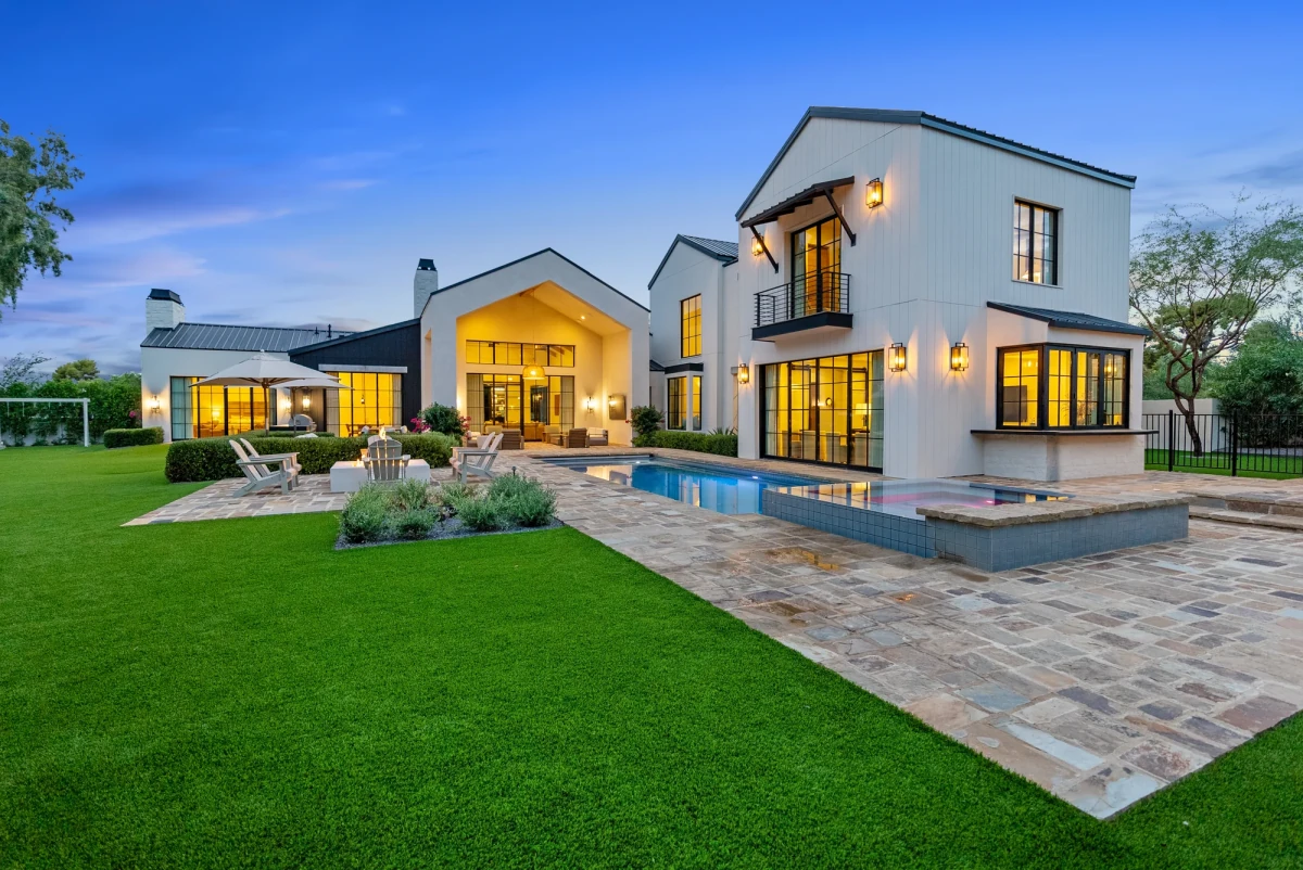 White luxury home, pool and landscaped lawn glowing at twilight