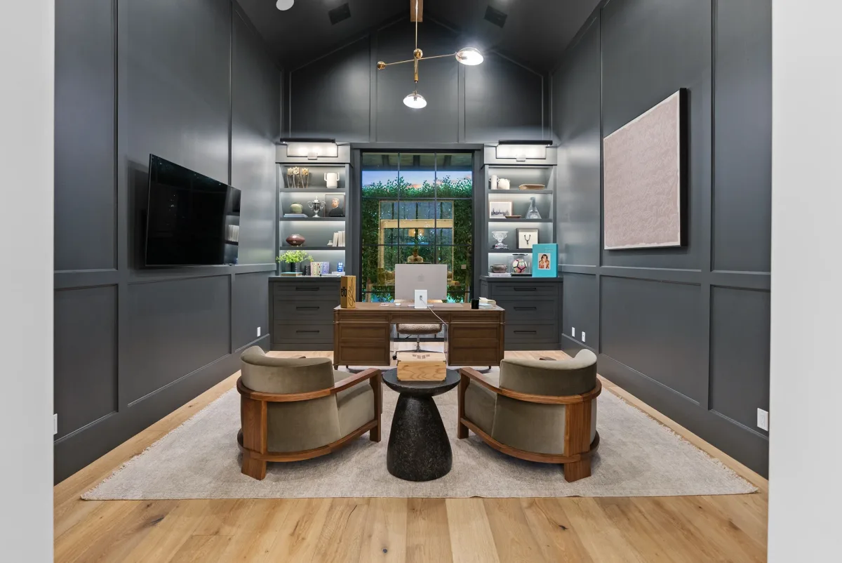 Dark paneled home office with two lounge chairs and illuminated shelving