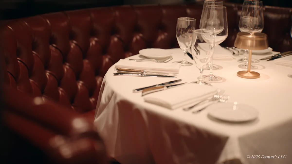 A set table with wine glasses beside red leather seating at Durant’s