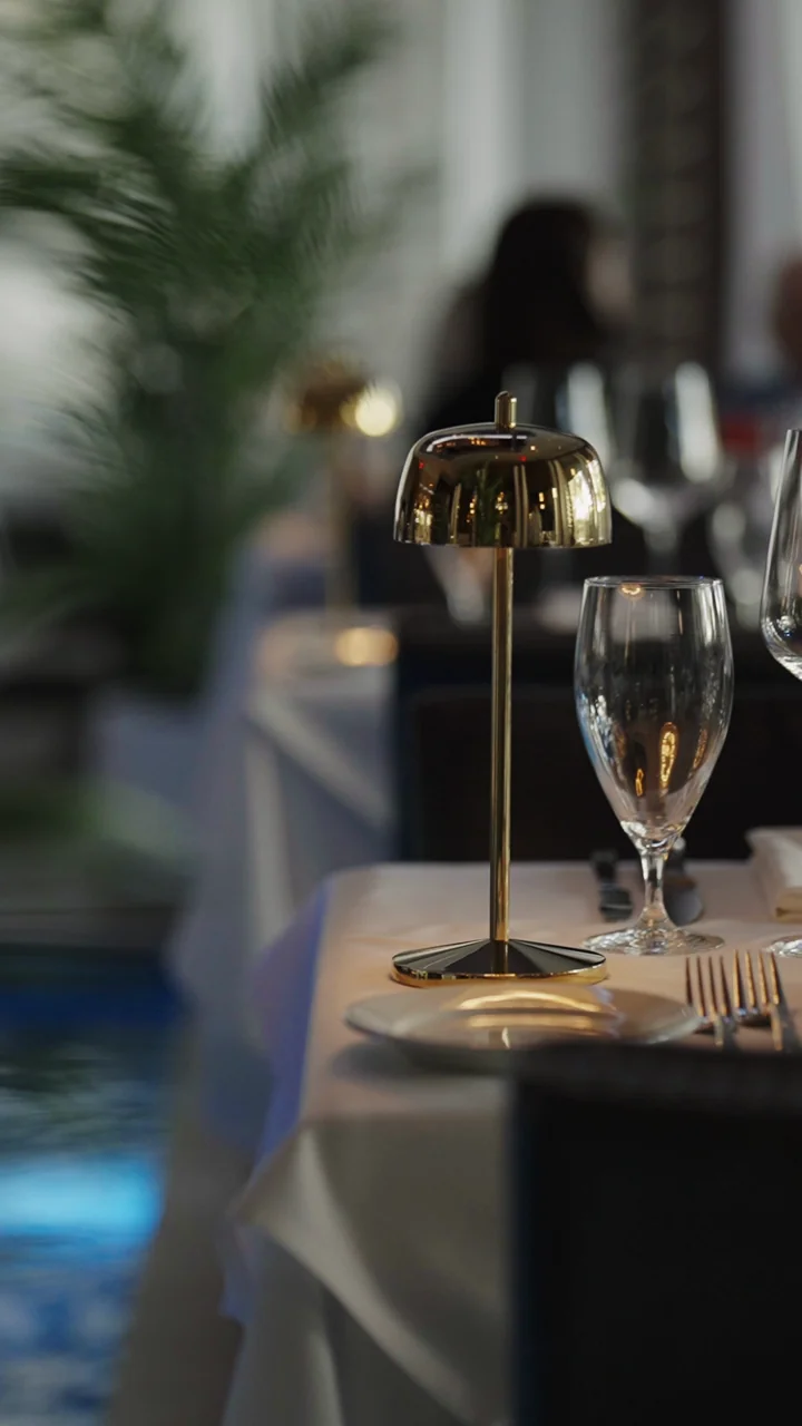 A set dining table with glasses and a small lamp beside a blue pool